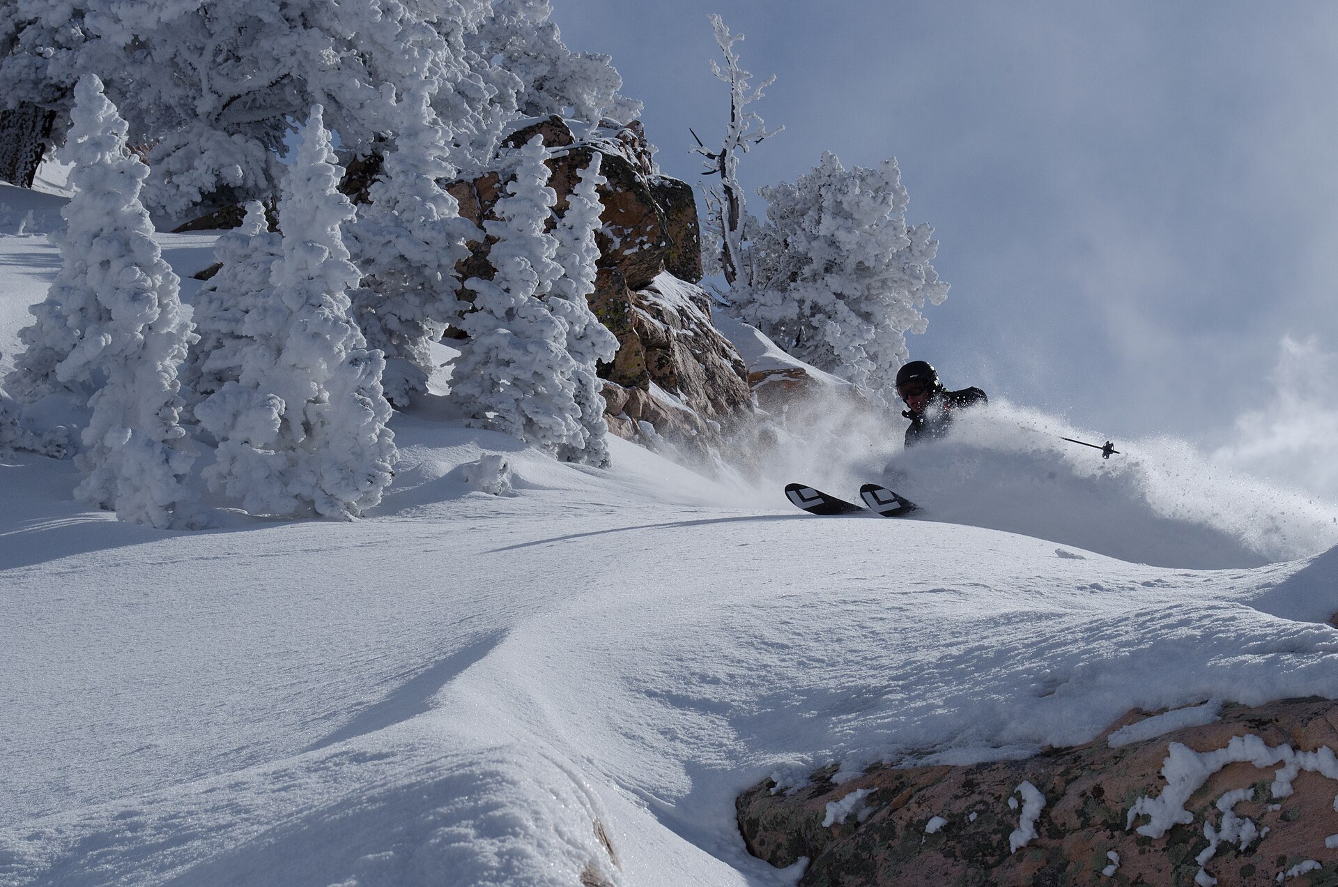 Skier laying a turn through deep spring powder at Snowbasin beneath cliffs